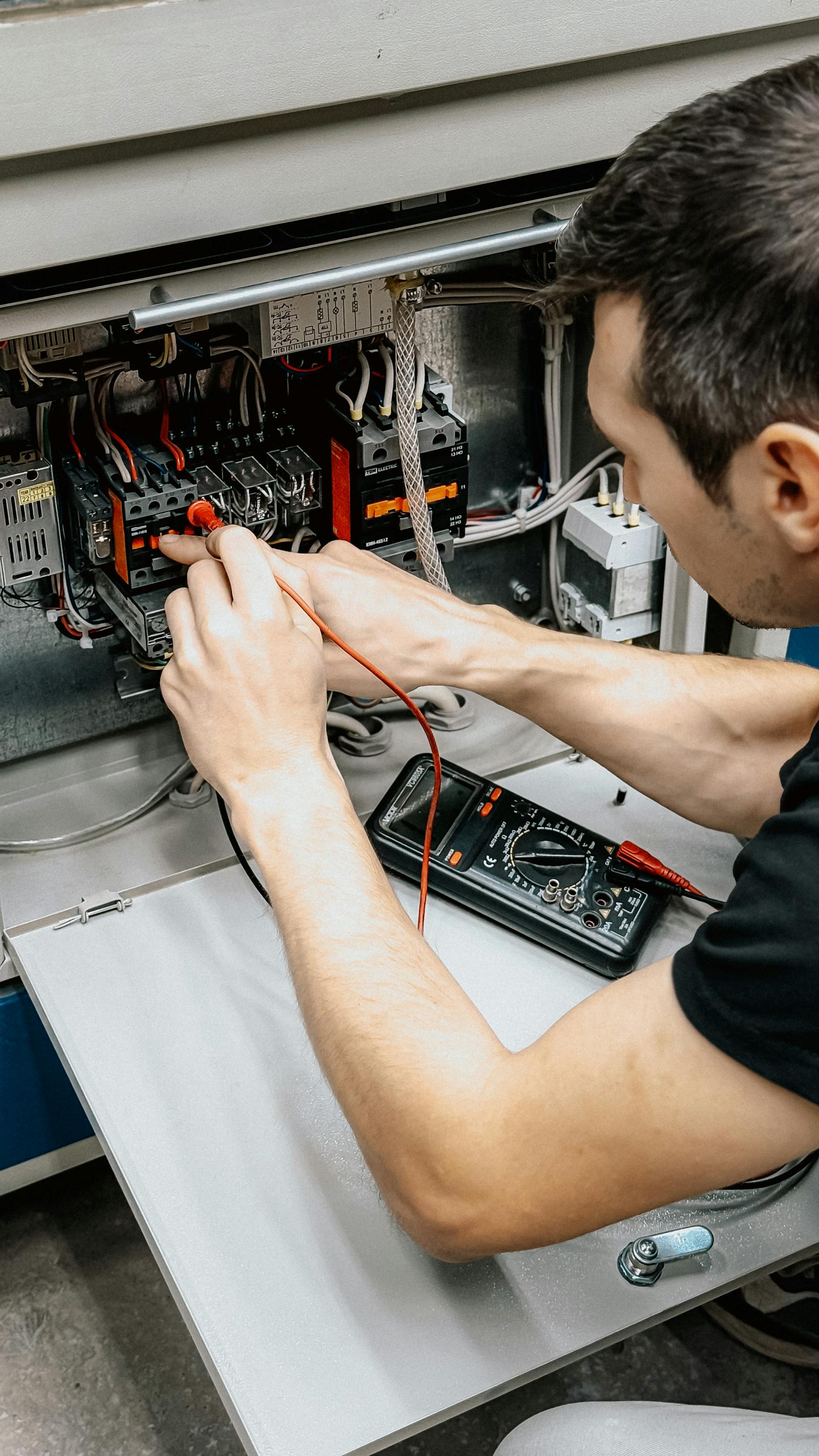 City and Guilds qualified electrician testing a control panel with a multimeter